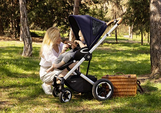 Frau kniet vor Kind im Kinderwagen der Firma cybex