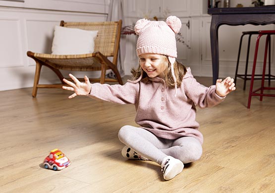 Kind sitzt auf dem Boden und spielt mit einem Auto.