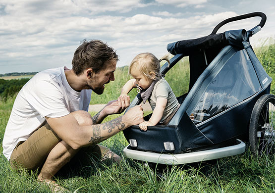 Mann im Gras beugt hilft einem Kind aus dem Fahrradanhänger der Firma Croozer